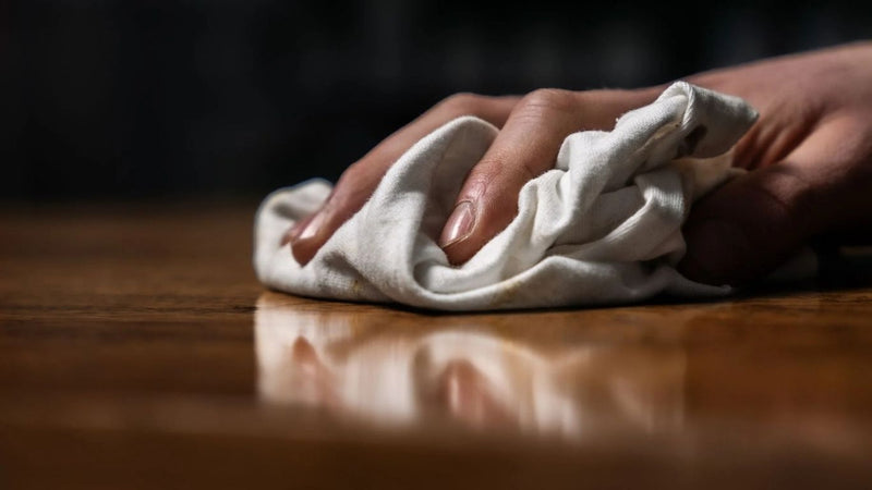 Wax polish being applied on a wooden flat surface with a soft white cloth